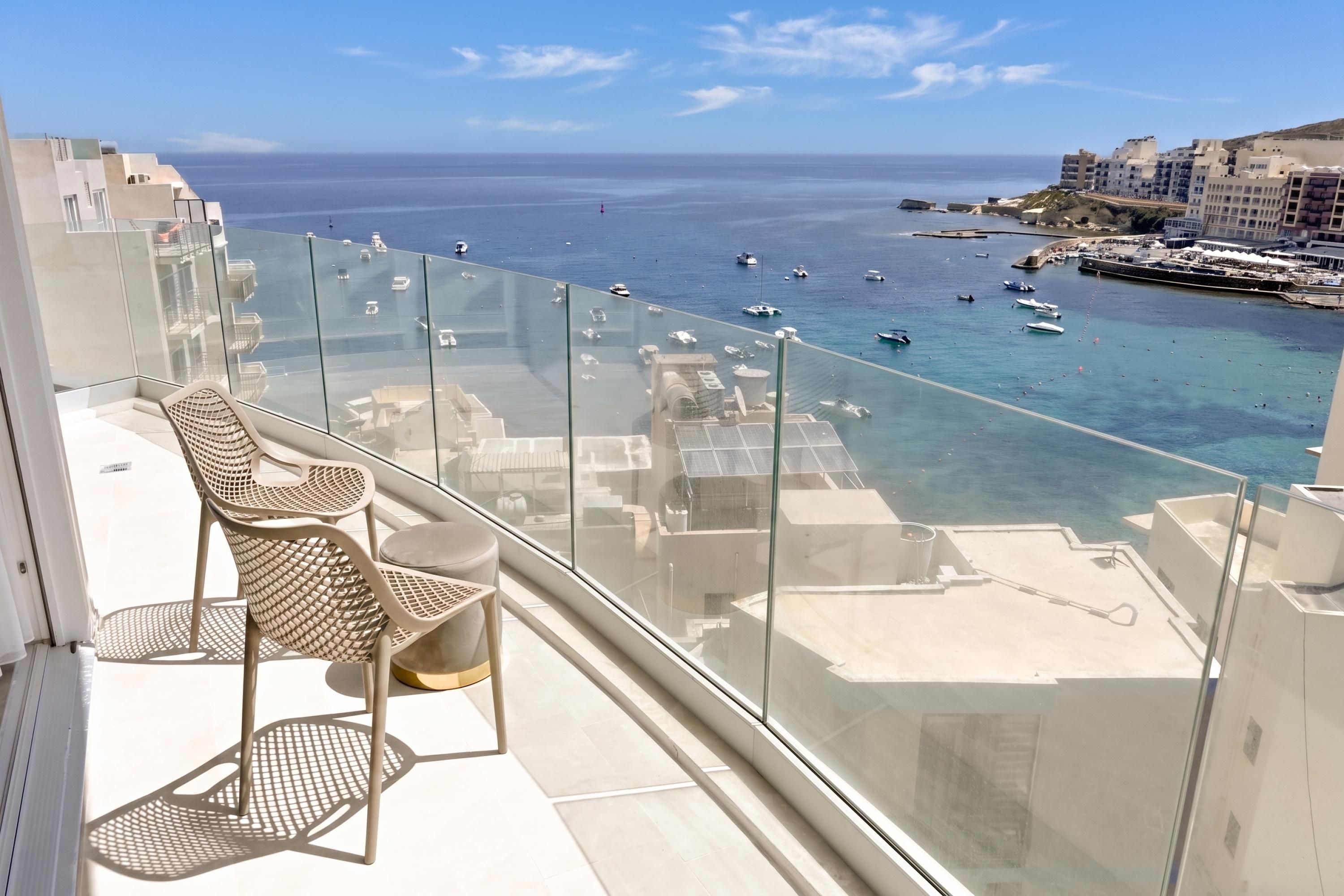 A balcony with a glass railing overlooking a marina with boats and a clear view of the sea.