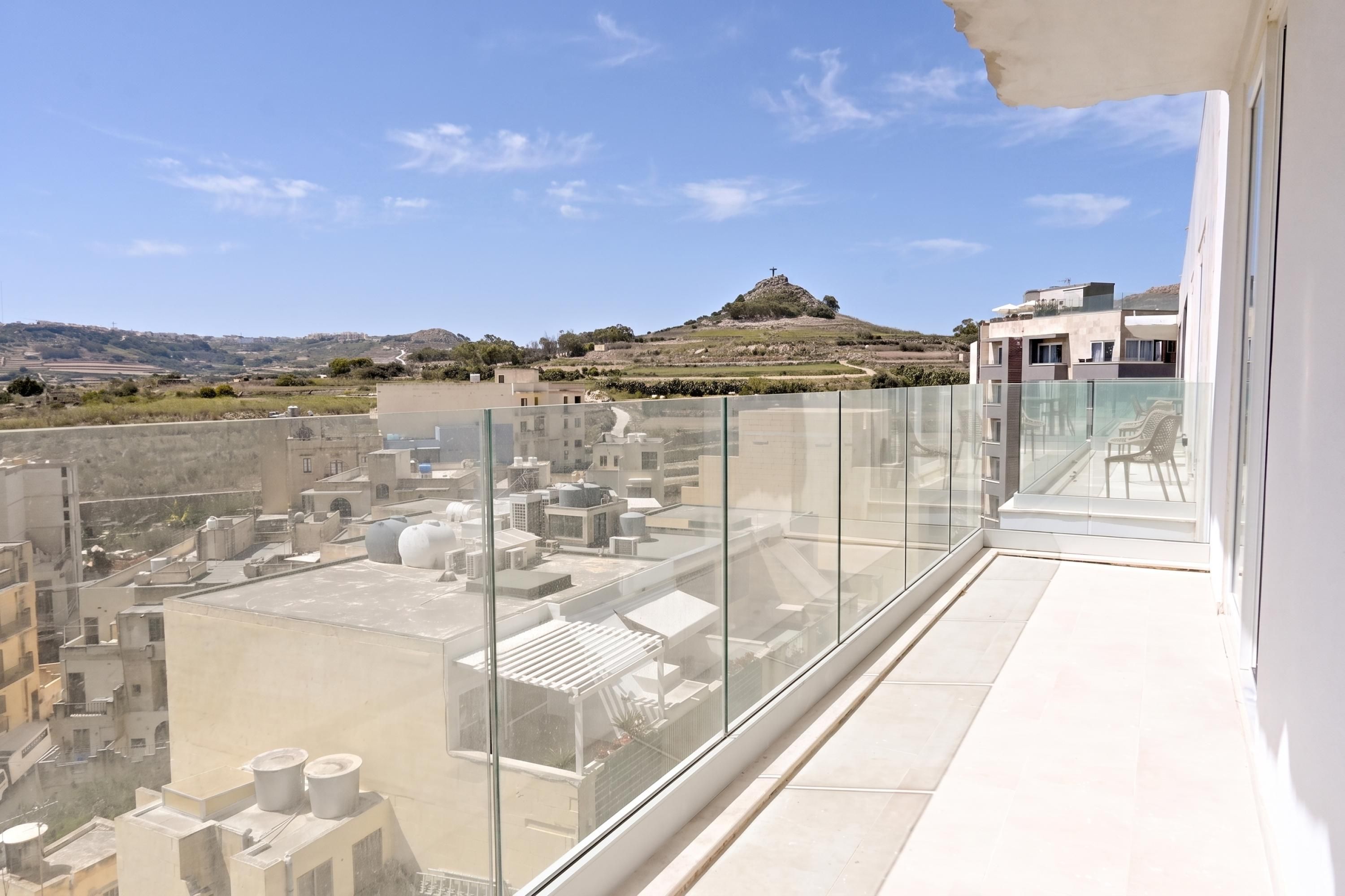 Terraza en la azotea con barandilla de vidrio, vista a un paisaje urbano y colinas al lejano.