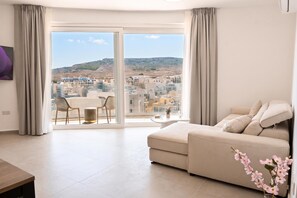 Una sala de estar moderna con un sofá, una mesa de comedor y vistas a un paisaje urbano a través de amplios ventanales.