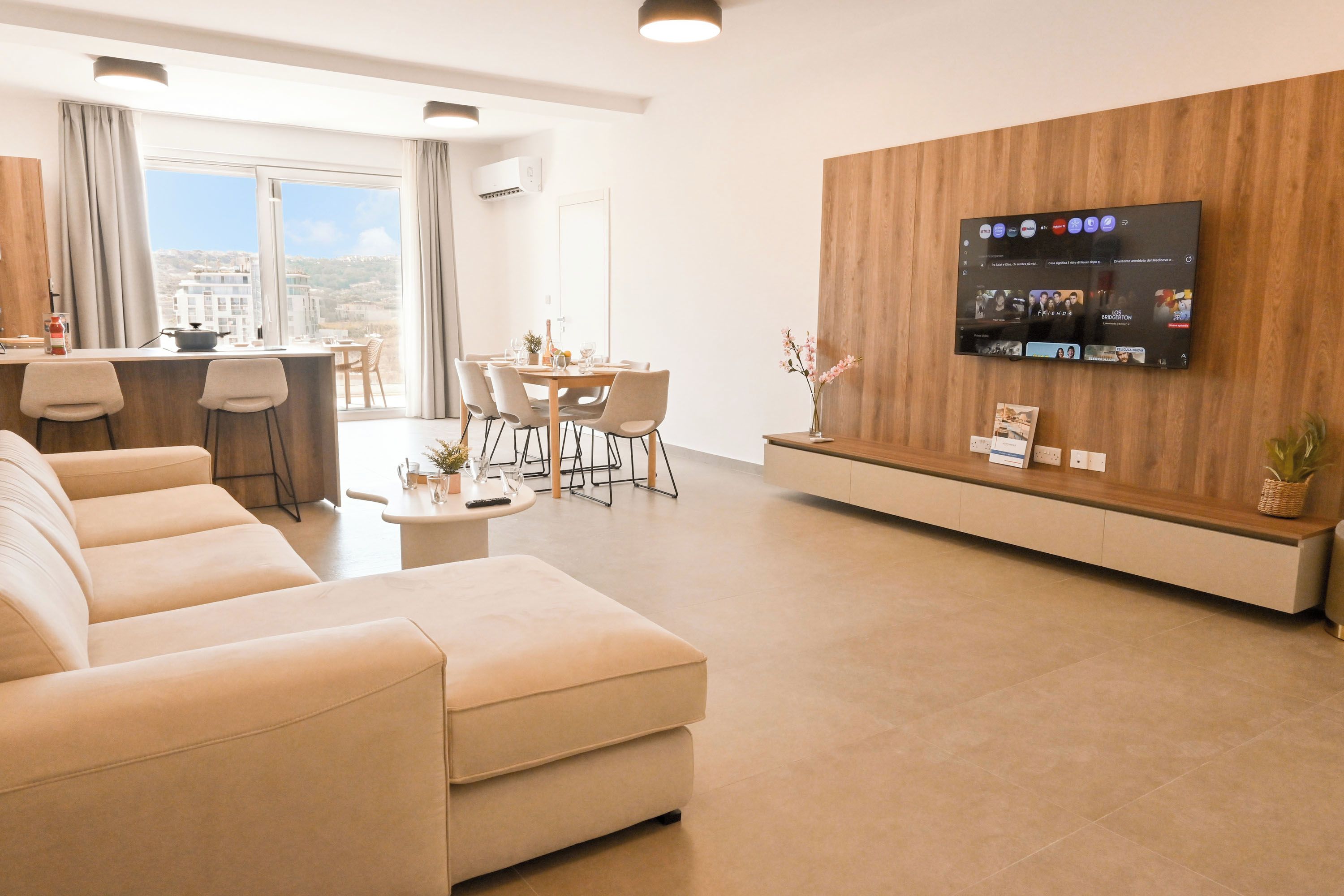 A modern living room with a sofa, dining area, and a TV mounted on a wooden wall.