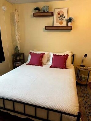 Une chambre à coucher comprenant un lit, des oreillers, une table de chevet, une lampe et des étagères murales décorées d’objets d’ornement.