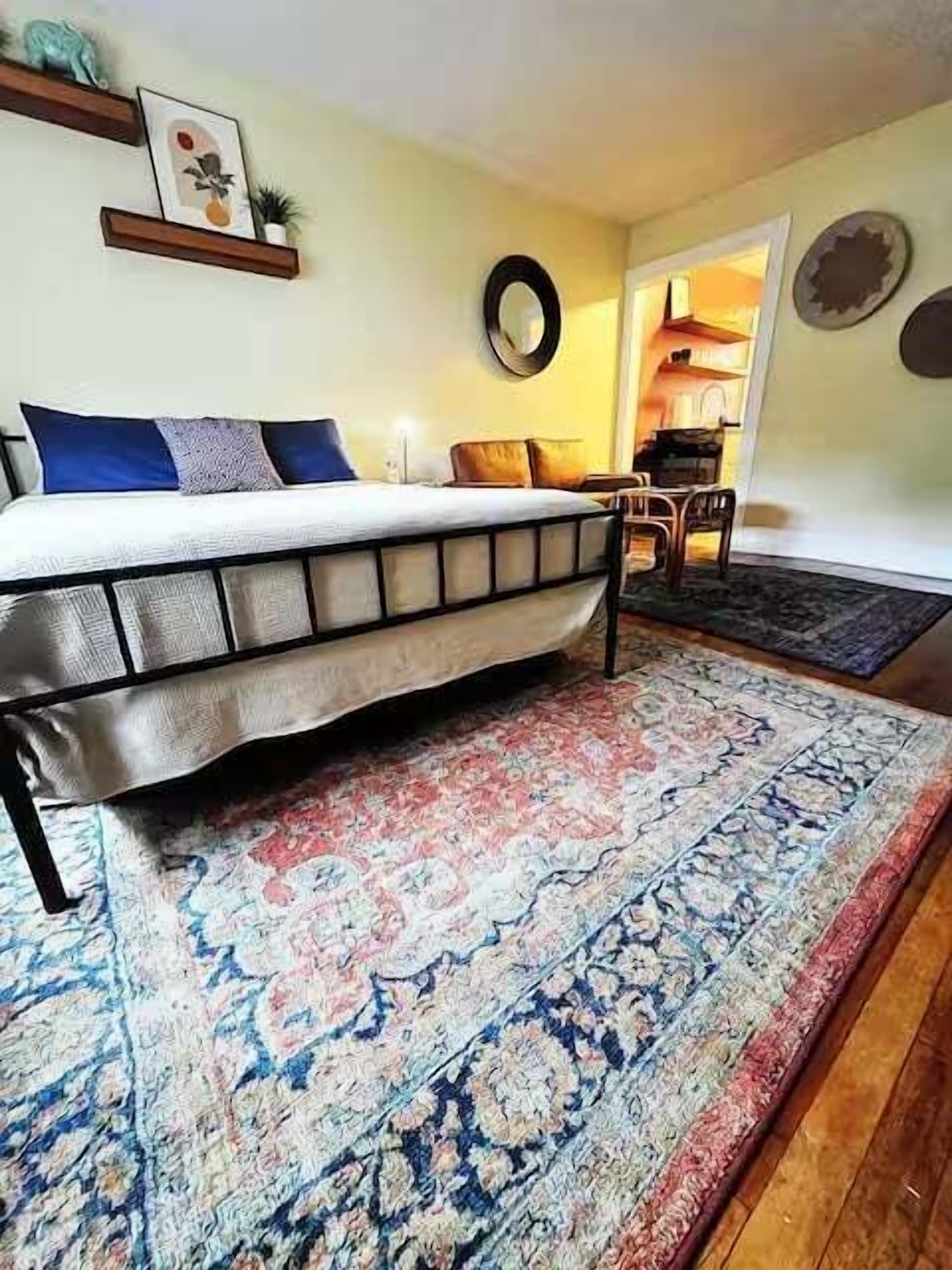 A bedroom with a bed, a rug, a chair, and a small table.