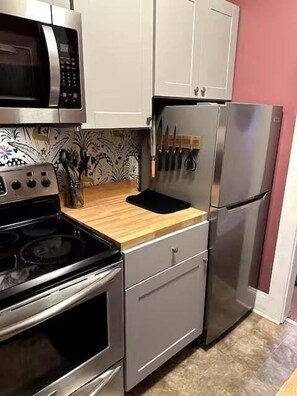 Eine kleine Küche mit Mikrowelle, Herd, Kühlschrank und einer Holzausziehtafel.