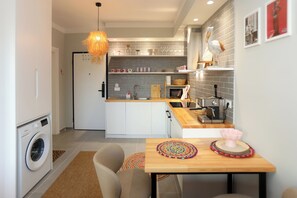 A compact kitchen with a washing machine, a dining table with chairs, and a hanging light fixture. - Cherry Studio Palm Radhime, Vlore, Albania (Vlore)