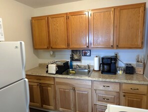 A kitchen with wooden cabinets, a refrigerator, a coffee maker, and a sink. - Marigold Flat - NEW! Downtown Ellsworth (Ellsworth)