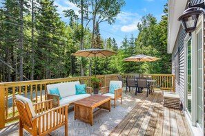 A wooden deck with outdoor furniture, including a sofa and chairs, and two umbrellas.
