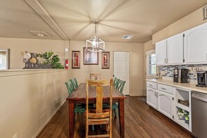 Una cocina con una mesa de comedor de madera, sillas verdes, armarios blancos y una lámpara colgante.