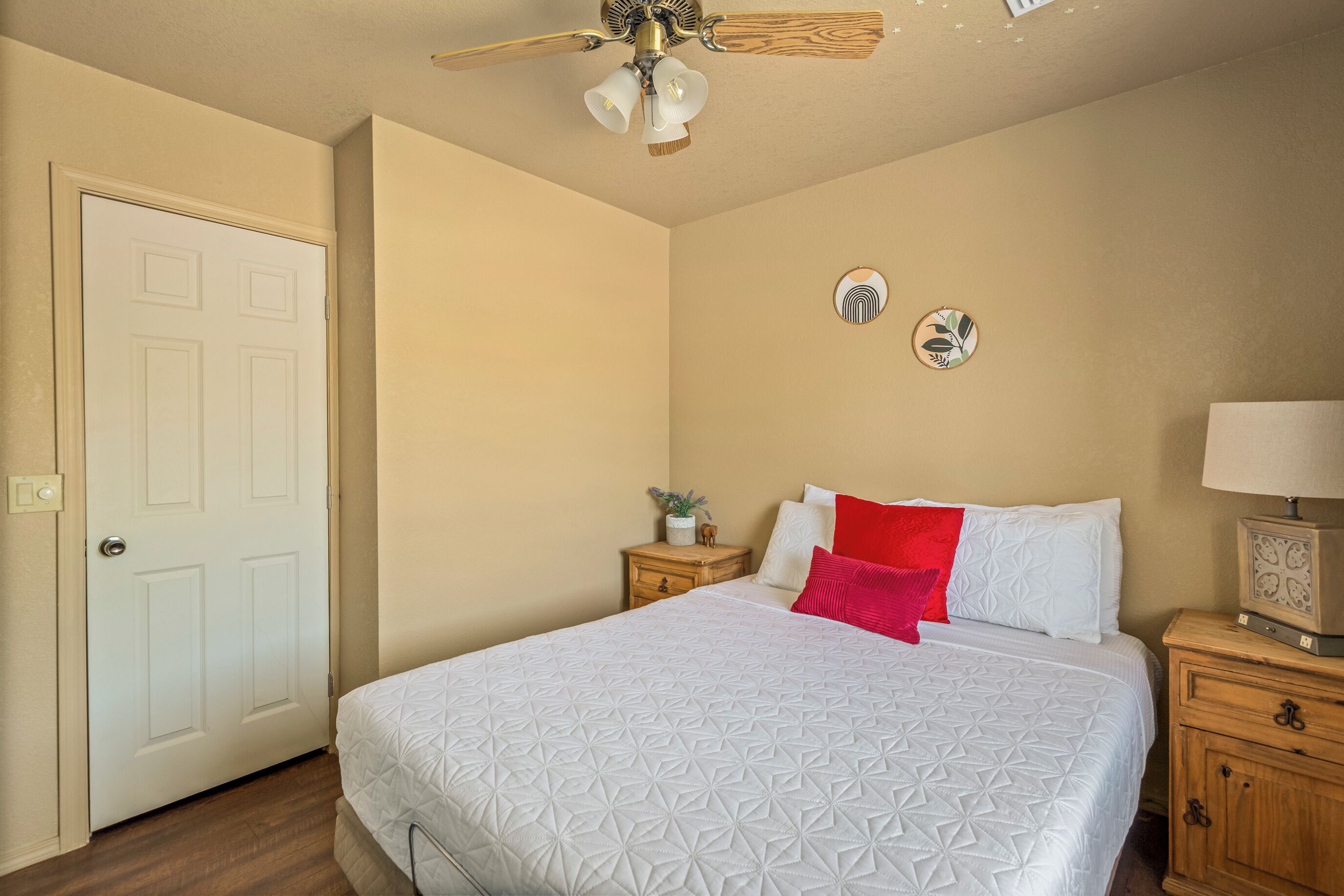 A bedroom with a bed, a nightstand, a lamp, a ceiling fan, and a door.