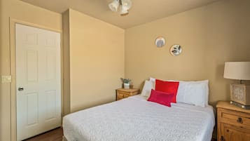 A bedroom with a bed, a nightstand, a lamp, a ceiling fan, and a door.