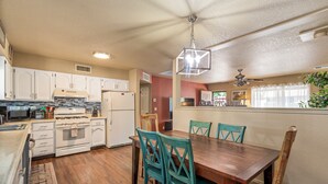 Une cuisine avec des meubles blancs, une cuisinière et un coin repas comprenant une table en bois et des chaises de couleur turquoise.