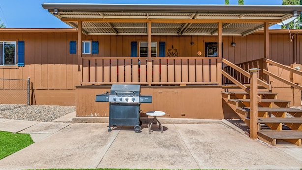 Un espace extérieur abrité comprenant un barbecue, une terrasse en béton et un escalier en bois.