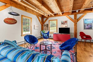 A spacious living area with a high wooden ceiling, a sofa set, a red entertainment unit, and a television. - The Barn on the Bagaduce - NEW! Waterfront (Sedgwick)
