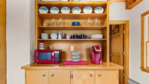 Een keuken met houten kastjes, een magnetron, een koffiezetapparaat en diverse servies en glazen.