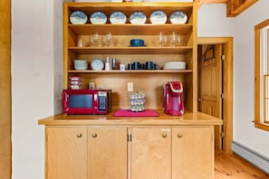 A kitchen with wooden cabinets, a microwave, a coffee maker, and various dishes and glassware. - The Barn on the Bagaduce - NEW! Waterfront (Sedgwick)