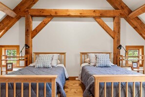 A bedroom with two wooden beds, a sloped ceiling, and a window with a view of greenery. - The Barn on the Bagaduce - NEW! Waterfront (Sedgwick)