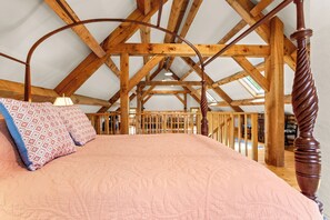 A bedroom with a wooden ceiling structure, a bed with a patterned bedspread, and a nightstand with a lamp. - The Barn on the Bagaduce - NEW! Waterfront (Sedgwick)
