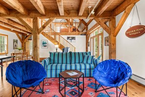A spacious room with a high ceiling, wooden beams, a striped sofa, two blue armchairs, a small table, and a rug. - The Barn on the Bagaduce - NEW! Waterfront (Sedgwick)