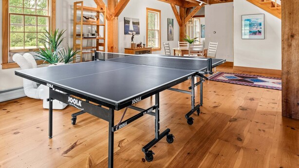 Een tafeltennistafel in een kamer met houten balken, een boekenkast en een trap.
