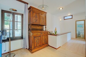 A room with a wooden cabinet, a window with a view, a ceiling light, and a mirror on the wall.