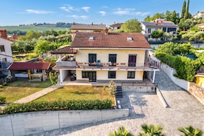 Une maison à deux étages, avec un toit en tuiles, un balcon et une allée pavée.