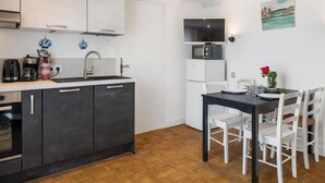 A compact kitchen with a microwave, sink, and cabinets. There is a dining area with a table and chairs. - Gîtes de France® - Between the Golf Course and the Sea (DIEPPE)