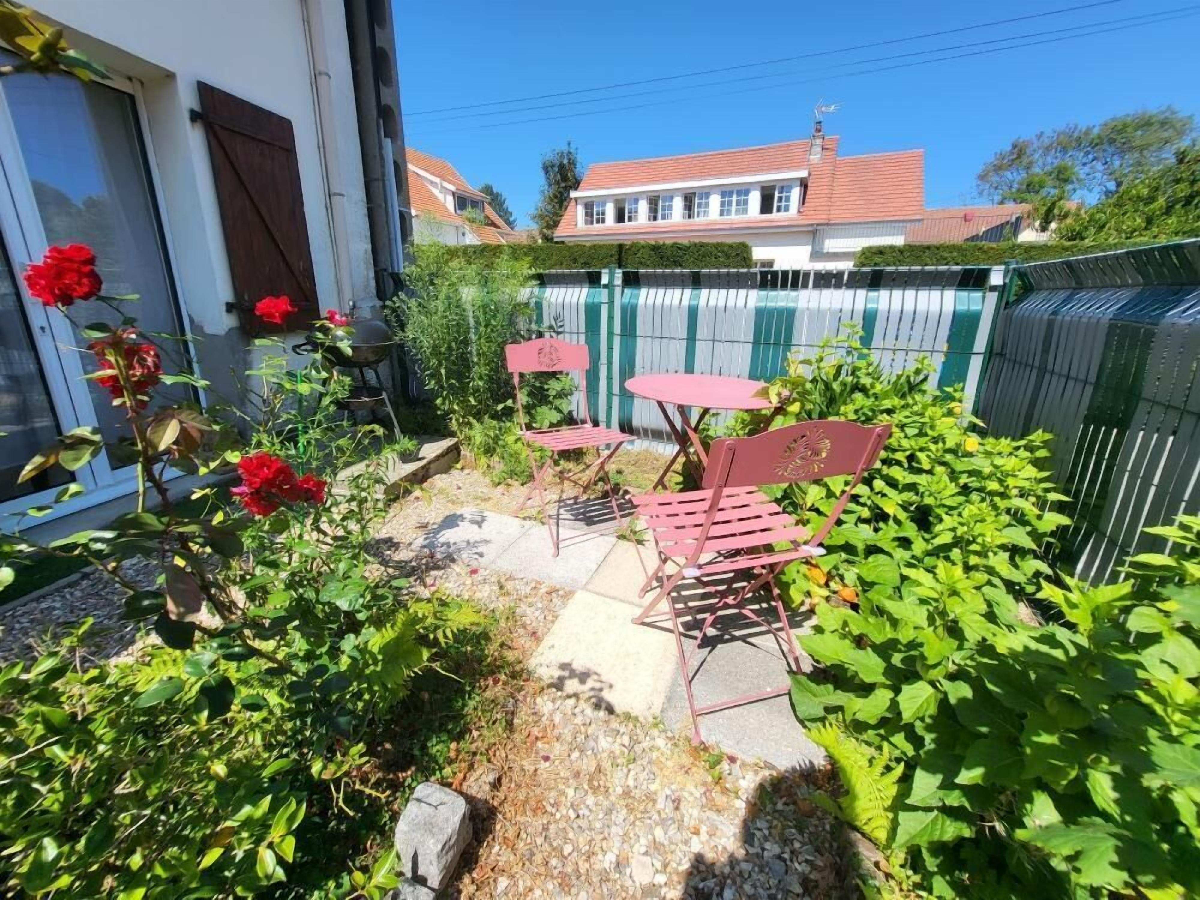 A patio with outdoor furniture, a garden with plants and flowers, and a house in the background.