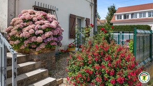 A residential building with a staircase leading to a door, a large flower arrangement on the steps, and a garden with red flowers. - Gîtes de France® - Between the Golf Course and the Sea (DIEPPE)