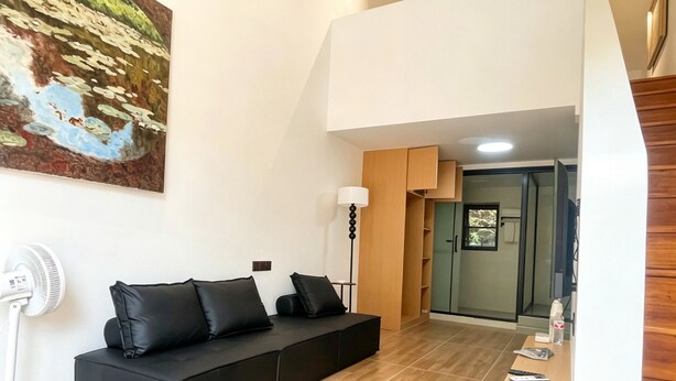 Un soggiorno moderno con un divano nero, una ventola a piantana e un quadro appeso al muro.