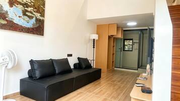 Una sala de estar moderna con un sofá negro, un ventilador de pie y un cuadro en la pared.