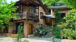 Una casa tradizionale in mattoni con un balcone in legno, gradini in pietra e un giardino fiorito.