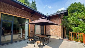 Un'area patio esterna con tavolo e sedie, un ombrellone grande e un edificio in mattoni con porte vetrate.