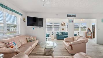 A spacious living room with a large flat-screen TV, comfortable seating, and a view of the outdoors.