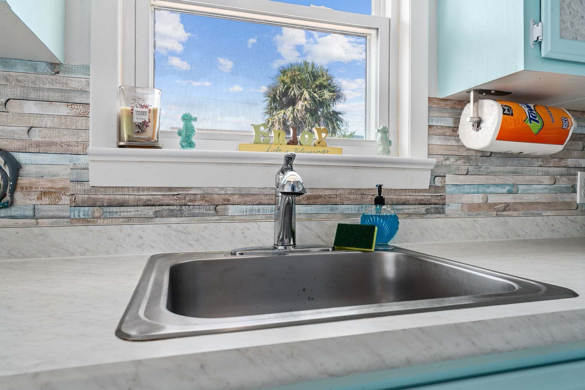 A kitchen with a stainless steel sink, a window with a view of palm trees, and a decorative item on the windowsill.