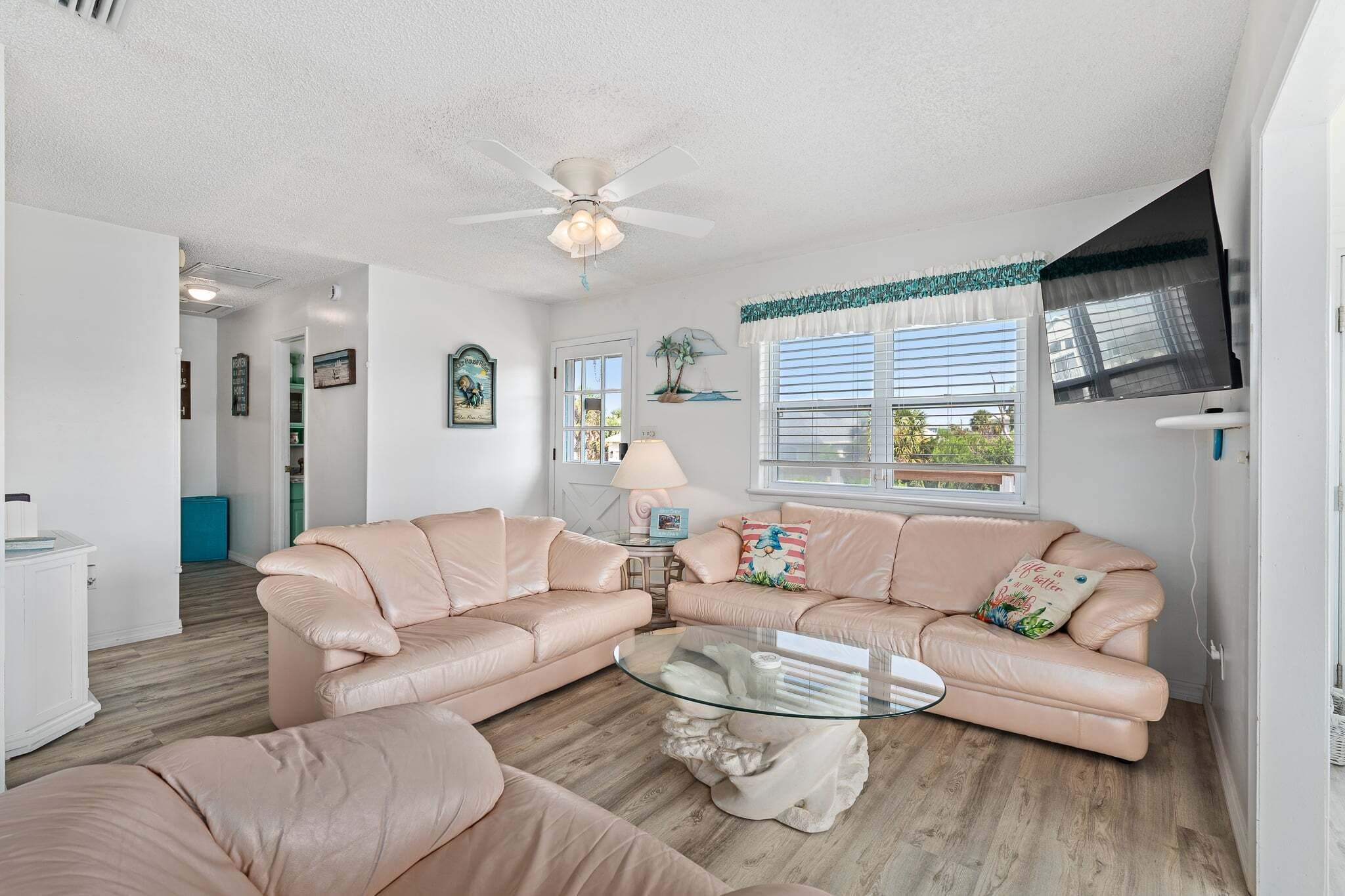 A living room with a sectional sofa, a glass coffee table, and a ceiling fan.