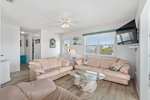 A living room with a sectional sofa, a glass coffee table, and a ceiling fan.