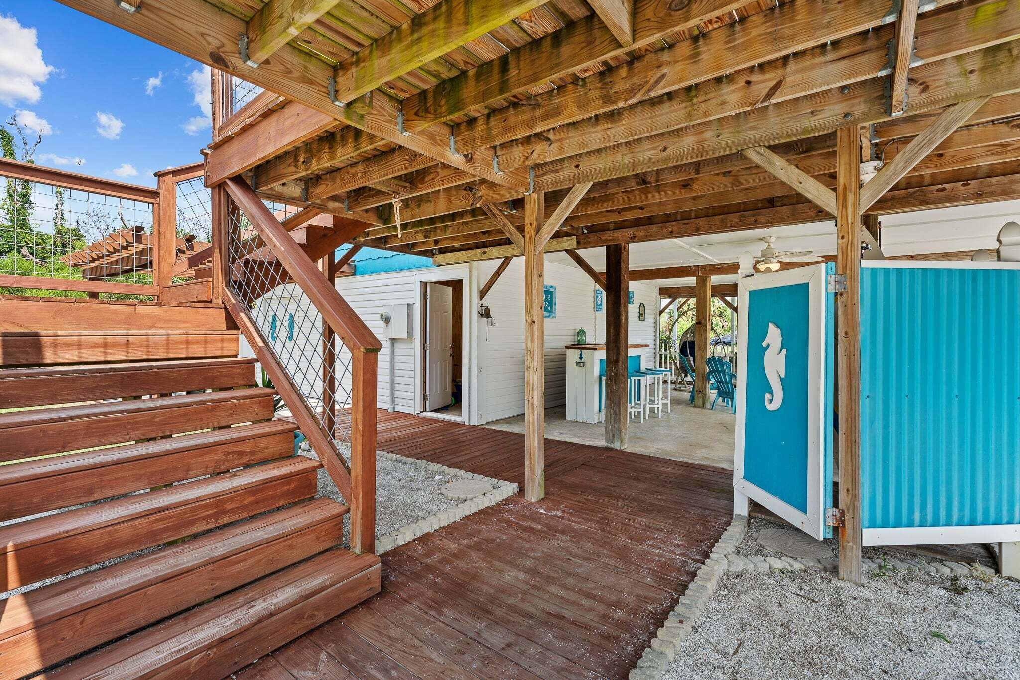 Ein überdachter Außenbereich mit Holzboden, einer Treppe und einem blauen Stauraum.