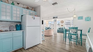 Eine Küche mit hellblauen Schränken, einem weißen Kühlschrank und einem Essbereich mit blaugrünen Stühlen und einem Tisch.