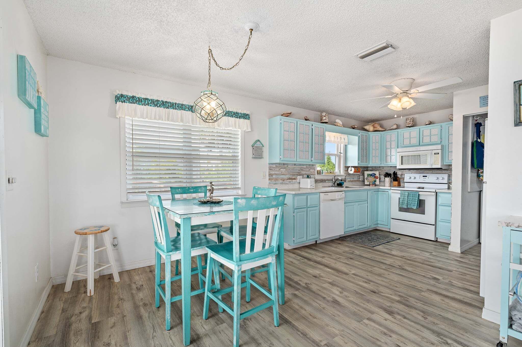 A kitchen with teal cabinets, a white countertop, and a dining area with teal chairs.