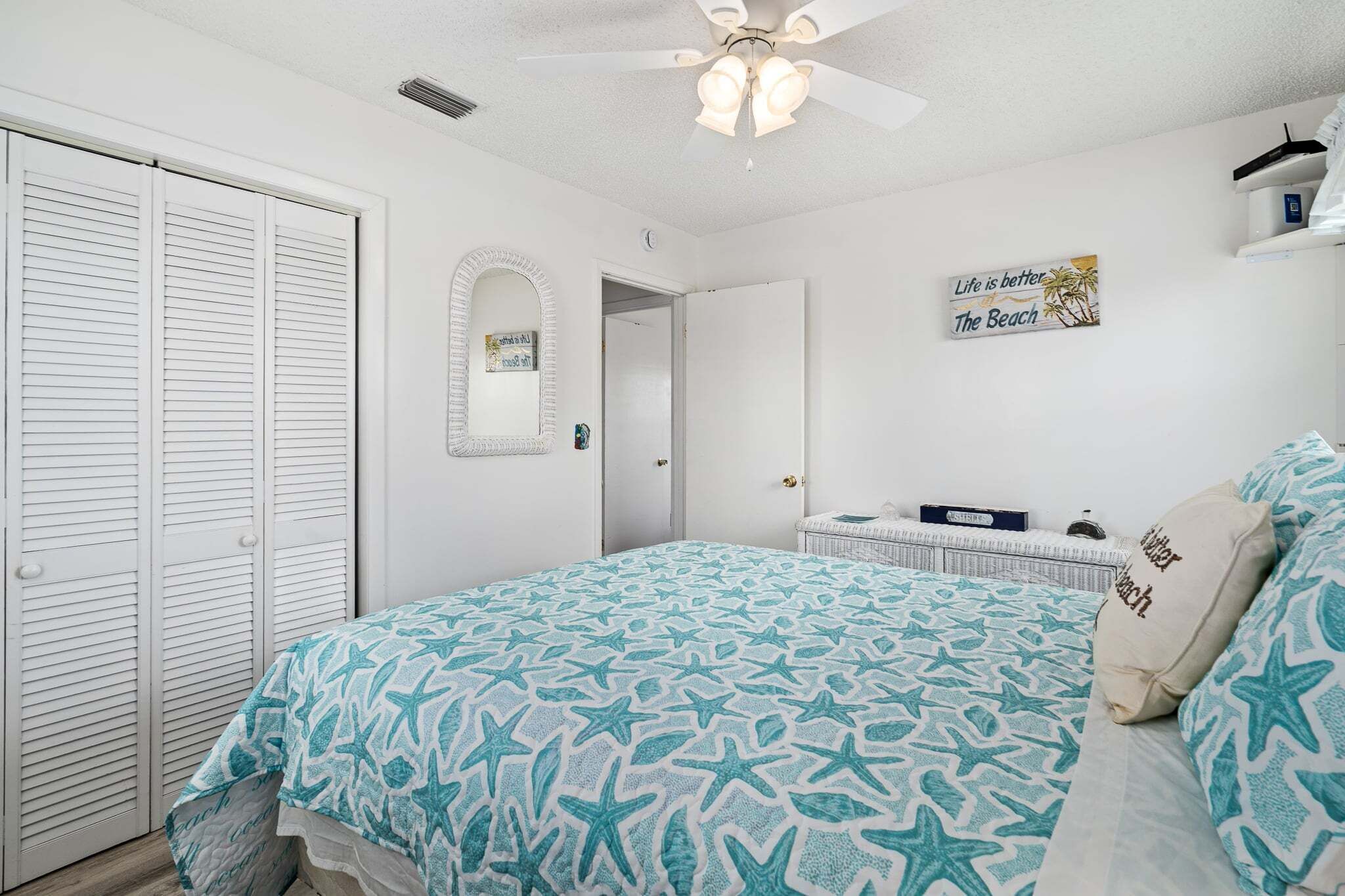A bedroom with a bed, a wardrobe, a ceiling fan, a mirror, and a sign on the wall.