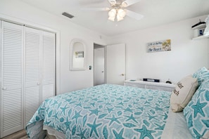A bedroom with a bed, a wardrobe, a ceiling fan, a mirror, and a sign on the wall.