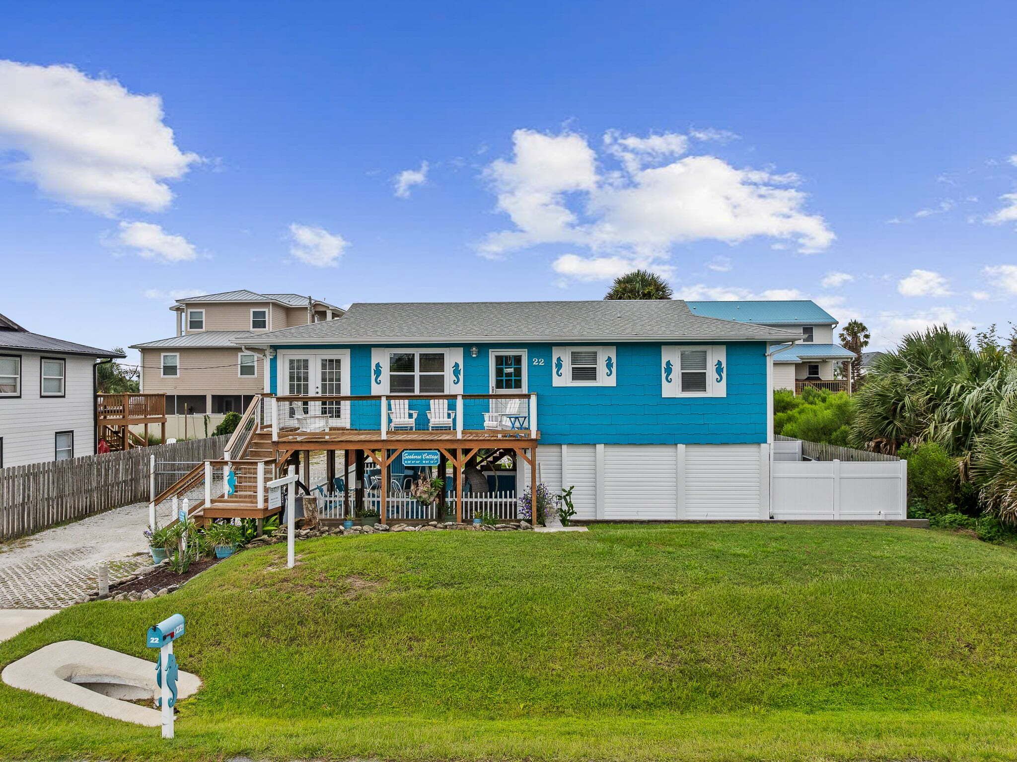 A two-story building with a blue exterior, a covered porch with chairs, and a mailbox marked with the number 22.