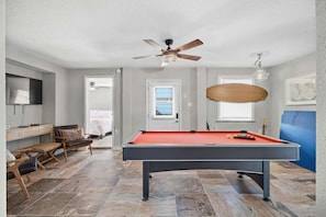 A pool table in a room with a ceiling fan, a television, and a door leading to another room.