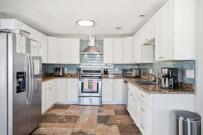 A modern kitchen with white cabinets, a stainless steel refrigerator, a built-in oven, a microwave, and a coffee maker.