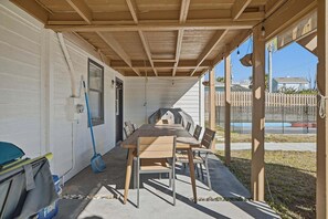 A covered patio with a table and chairs, a broom, and a trash bin.