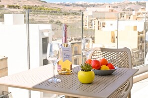 Un balcon avec une table dressée pour deux personnes, agrémentée d’une bouteille de vin, de deux verres et d’un saladier de fruits.