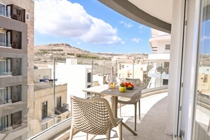 Un balcon avec une table, des chaises et un saladier rempli de fruits.