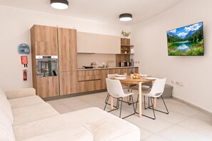 A modern kitchen with wooden cabinets, a dining table with chairs, and a painting of a mountain landscape. - Modern Seaside Apart in Marsalforn - 5C, Marsalforn Iz-Zebbug Gozo, Malta (Marsalforn Iz-Zebbug Gozo)