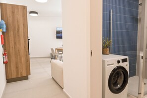 A laundry room with a washing machine, a fire extinguisher, and a small table with a chair. - Modern Seaside Apart in Marsalforn - 5C, Marsalforn Iz-Zebbug Gozo, Malta (Marsalforn Iz-Zebbug Gozo)