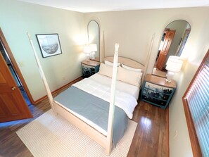 Ein Schlafzimmer mit Himmelbett, zwei Nachttischen mit Lampen, einem großen Spiegel und einem gerahmten Bild an der Wand.