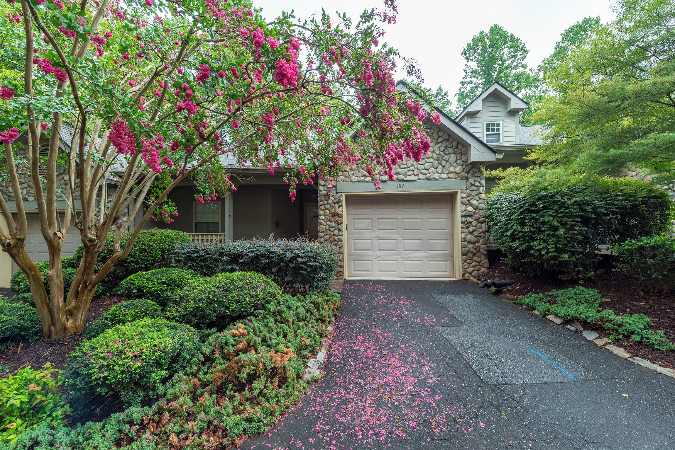 A residential property with a stone facade, a garage, and a driveway with scattered flower petals.